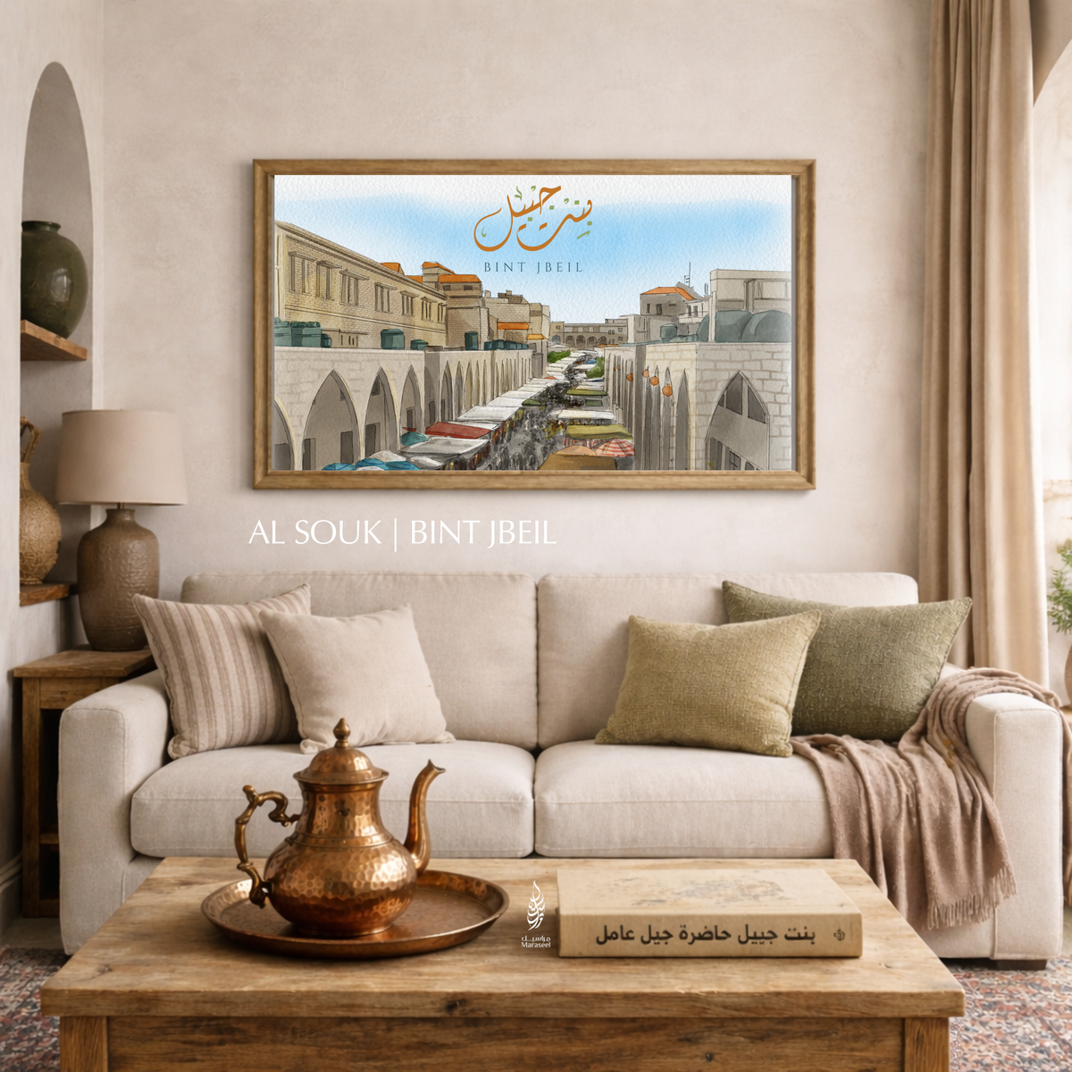 Living room with a framed picture of a souk scene on the wall of Bint Jbeil, a beige sofa with decorative pillows, and a wooden coffee table with a teapot. Art print of Bint Jbeil South Lebanon