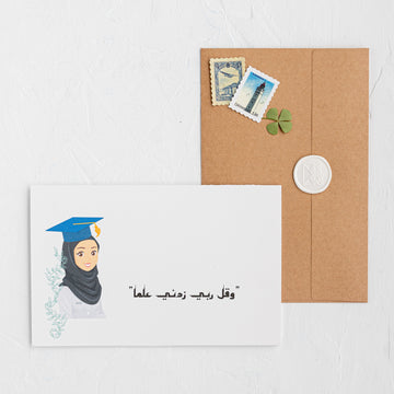 Graduation-themed card with a portrait of a person wearing a graduation cap and gown, placed on a white surface with a brown envelope and stamps.