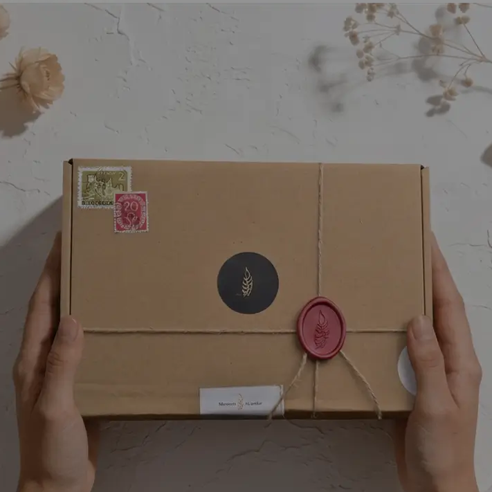 Person holding a cardboard box with decorative elements on a textured surface with flowers and a spool of twine.