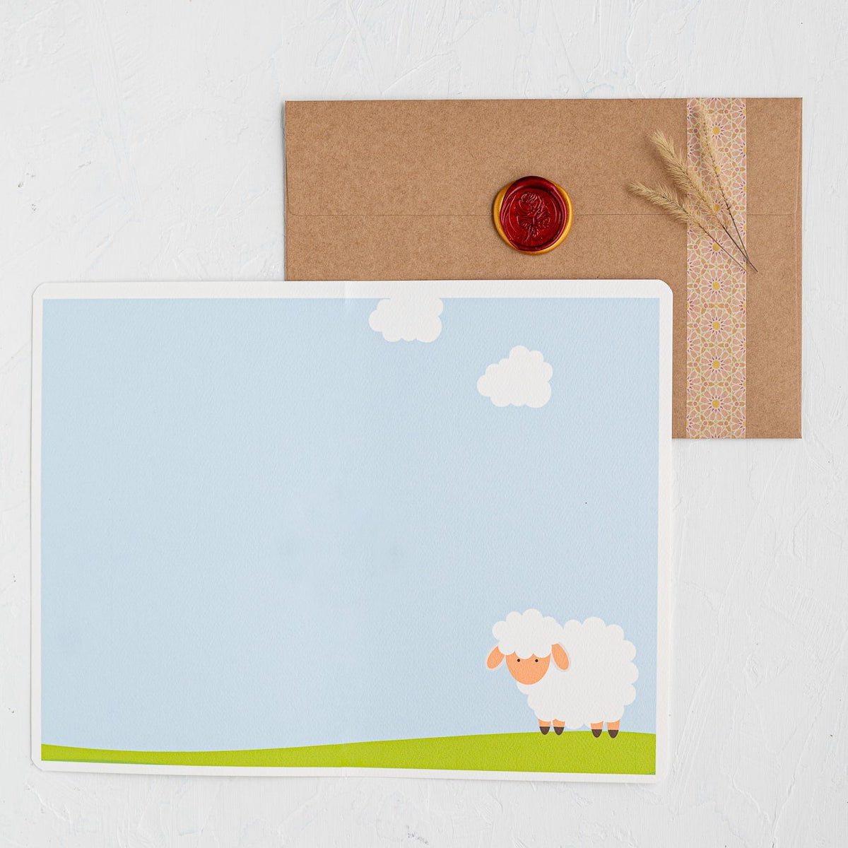 Greeting card with a sheep illustration on a blue sky background, accompanied by a brown envelope.