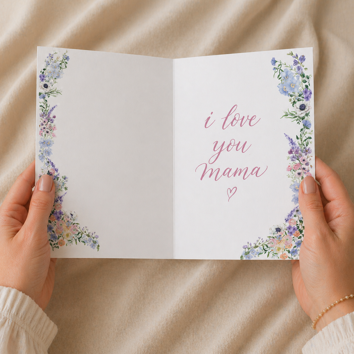 Card with 'I love you Mama' text held by hands on a beige fabric background