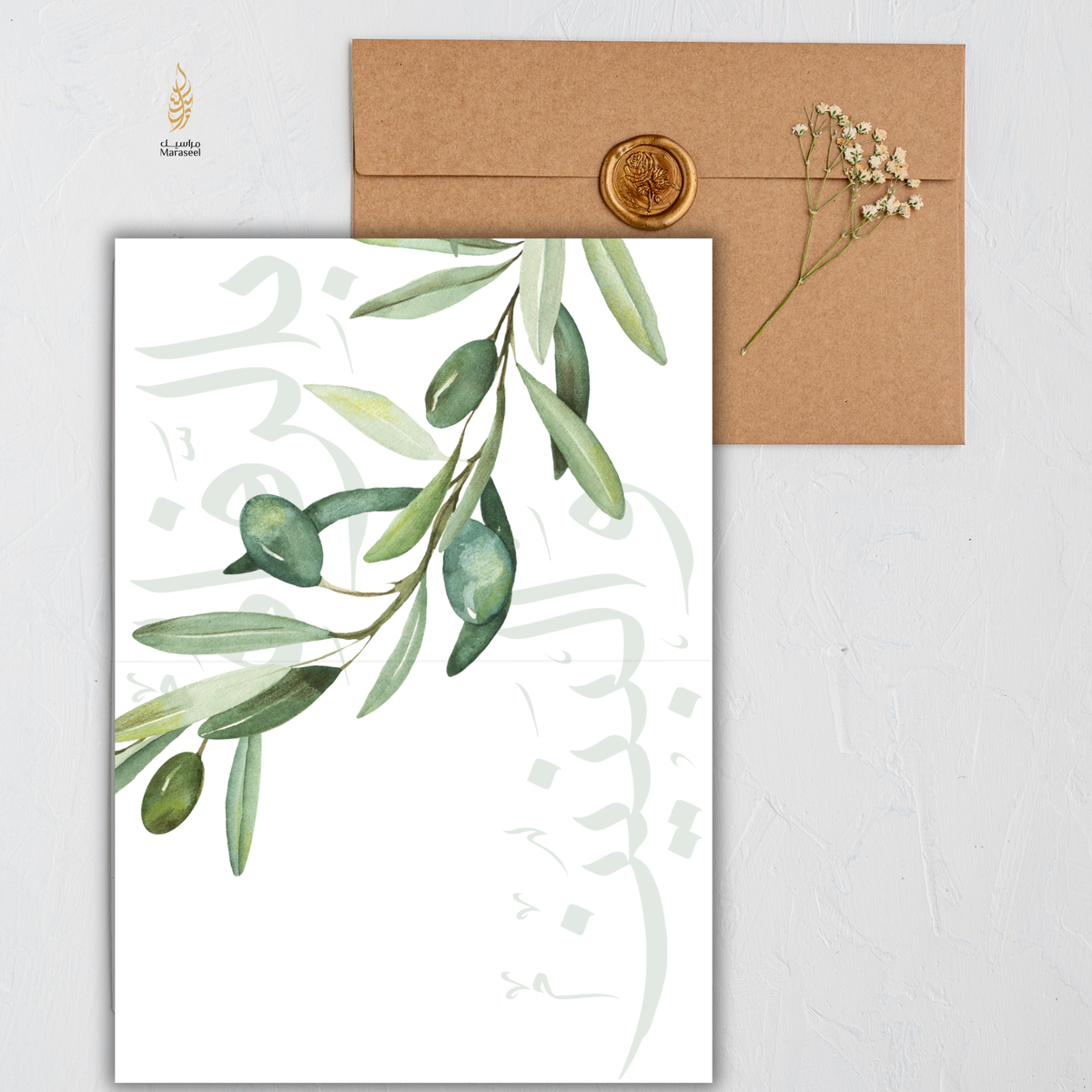 A watercolor olive branch printed card with elegant Arabic calligraphy on a white background, shown with a brown kraft envelope sealed with a gold wax stamp and a small sprig of baby's breath on a light textured surface.