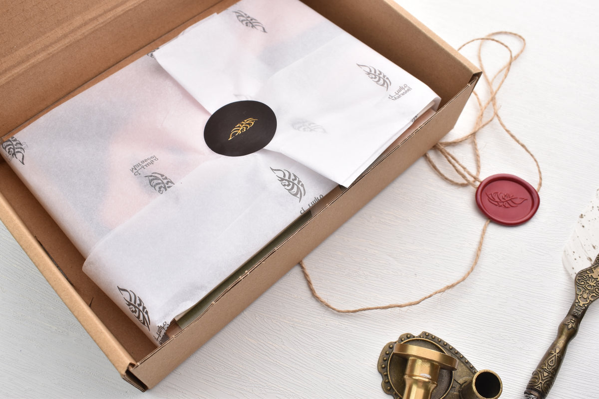 An opened Maraseel card set box: the cards wrapped in leaf-printed tissue paper, closed with a gold leaf sticker