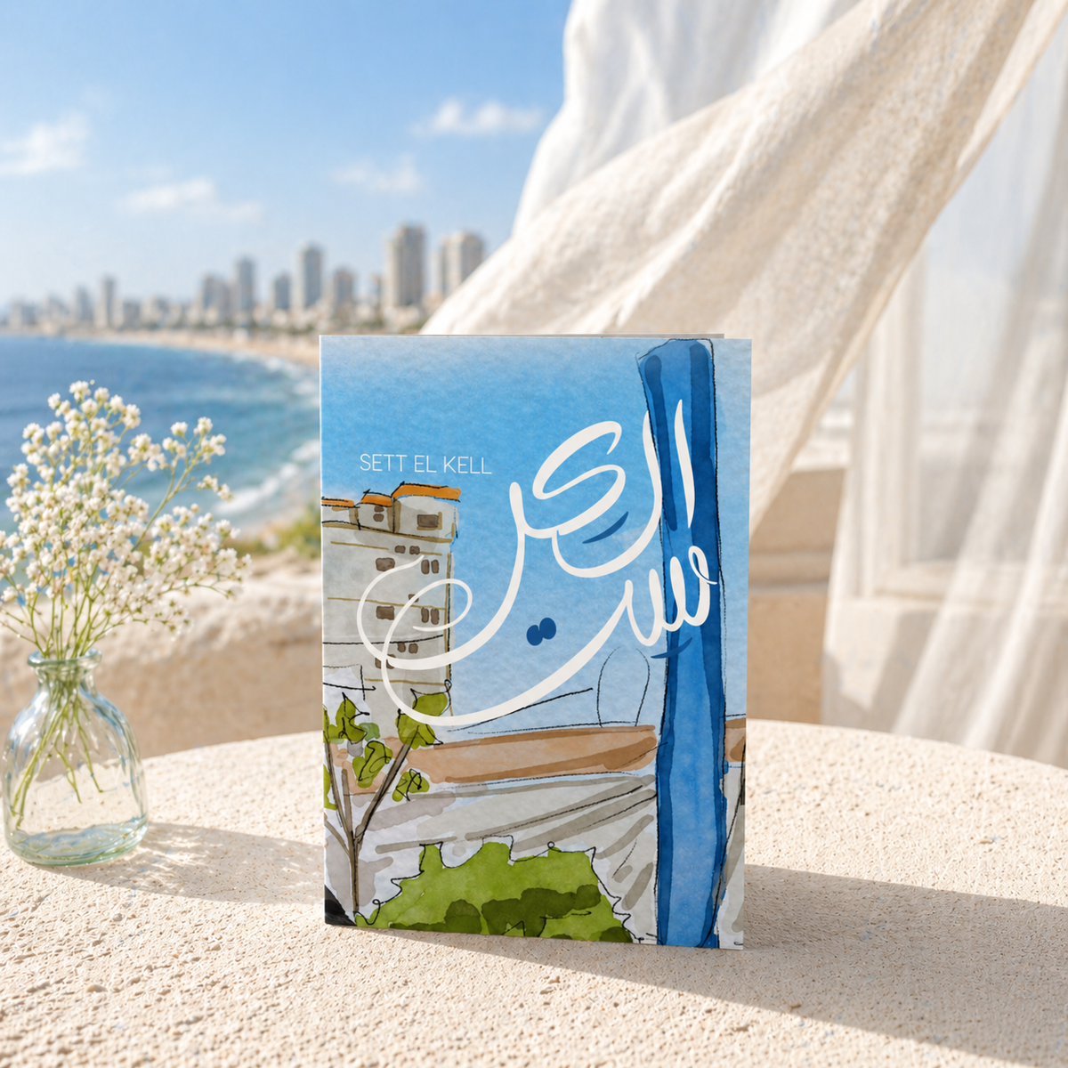 Book with beach scene cover on a sandy surface with ocean and cityscape in the background